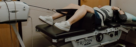 Person lying on a Triton DTS traction therapy table with straps securing the lower body, receiving spinal decompression treatment in a clinical setting