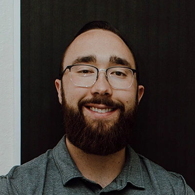 Jacob Covert wearing a gray collared shirt, positioned against a dark vertical panel background